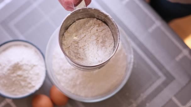 Zbliżenie koncepcji piekarni - kobieta przesiewać mąkę przez sito metaliczne do szklanej misy do pieczenia — Wideo stockowe