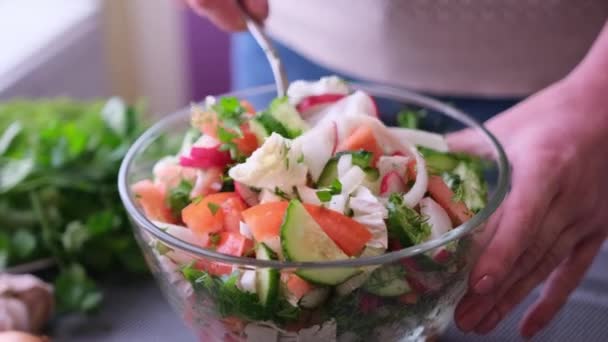 Woman mixes a salad of vegetables in glass bowl - tomatoes, cucumbers, onion, parsley — Vídeos de Stock