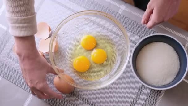Woman is crushing eggs into glass bowl and making dough — Vídeo de stock