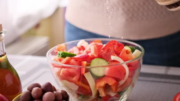 Greek salad preparation series concept - woman salting chopped vegetables in a glass bowl — Stock video