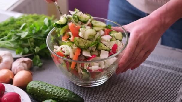 Woman mixes a salad of vegetables in glass bowl - tomatoes, cucumbers, onion, parsley — Wideo stockowe