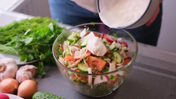 Woman adding sour cream to mixed salad of vegetables - tomatoes, cucumbers, onion, parsley — стоковое видео