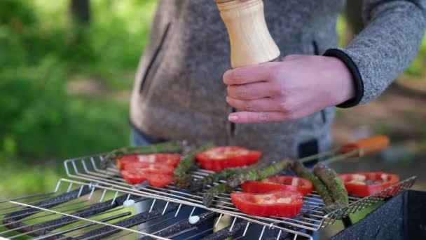 Making grilled vegetables - adding pepper and and spices to Asparagus and red pepper on a charcoal grill — Stock video