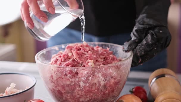 Adding water to minced meat with onion and spices in a glass bowl making cutlets — Vídeos de Stock
