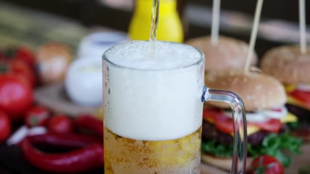 Pouring beer into glass mug with Cheeseburgers served with french fries on background — Αρχείο Βίντεο