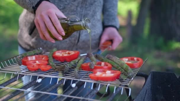 Robienie grillowanych warzyw - nalewanie oliwy z oliwek na szparagi i czerwonej papryki na grillu węglowym — Wideo stockowe