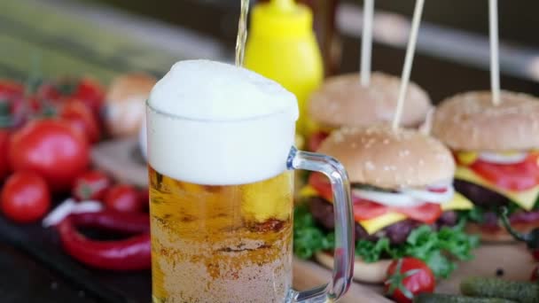 Pouring beer into glass mug with Cheeseburgers served with french fries on background — Stockvideo