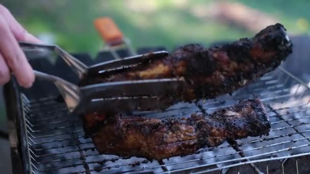 Lançando deliciosa carne ou costelas de porco fritando em uma grelha de carvão com pinças — Vídeo de Stock