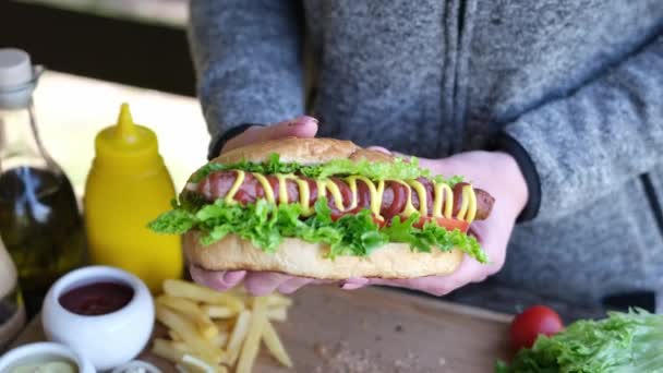 Woman holding fresh made hotdog with mustard and ketchup outdoors — Stock Video