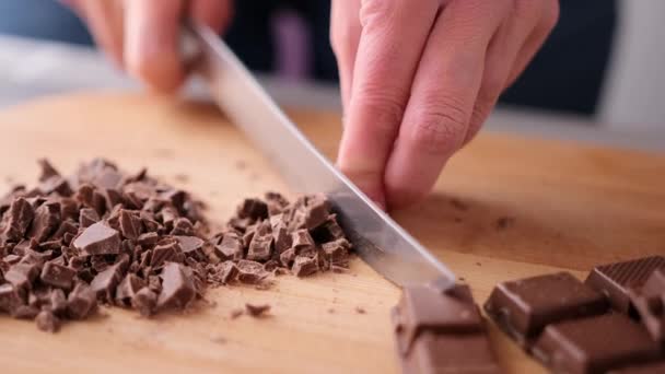 Женщина режет черный темный шоколад на деревянной доске — стоковое видео