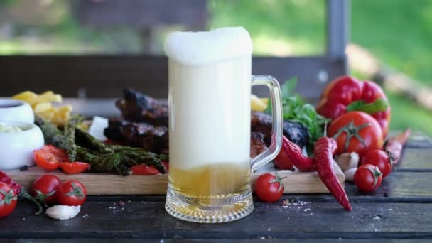 Despeje cerveja em caneca de vidro com deliciosas costelas de carne de vaca ou porco no fundo — Vídeo de Stock