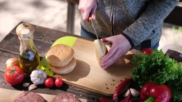 木の板の上にナイフで半分のハンバーガーパンを切った女性 — ストック動画