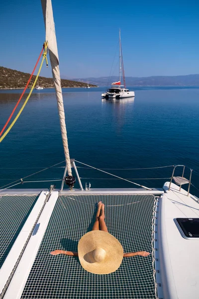 Beautiful young blond woman in bikini laying on catamaran bow at sunny summer day.