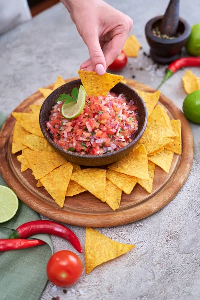 freshly made salsa dip sauce with nacho chips on wooden board.