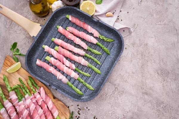 cooking aspargus covered with bacon on a grill frying pan.