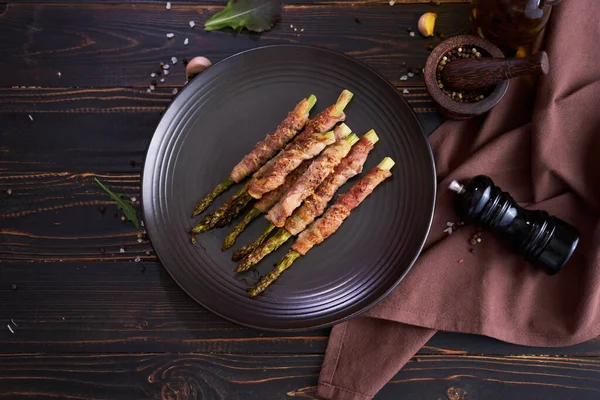 Baked Aspargus Covered Bacon Black Ceramic Plate Wooden Kitchen Table — Foto Stock