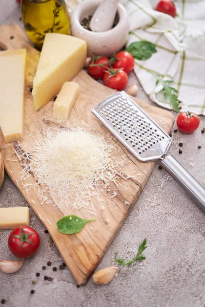 Parmesan cheese and grater on a wooden cutting board.