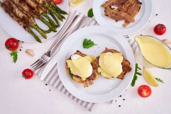 Tasty eggs Benedict, hollandaise sauce and aspargus covered with bacon.