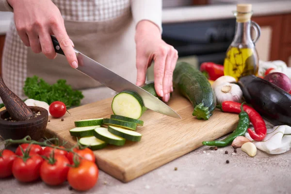 Woman slicing zucchini on wooden cutting board at domestic kitchen.