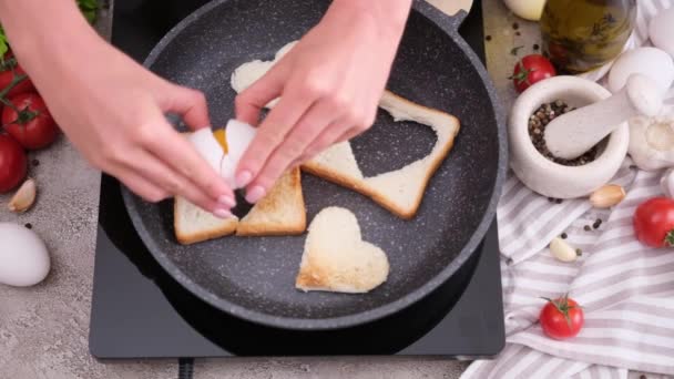 女性はトーストパンに卵を打ち込み 心臓の形をした穴を開けて自宅のキッチンで熱々のフライパンでトーストを食べる — ストック動画