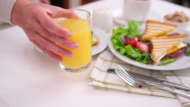 おいしい朝食 女性はサンドイッチとテーブルの上に新鮮なオレンジジュースのガラスを置きます — ストック動画