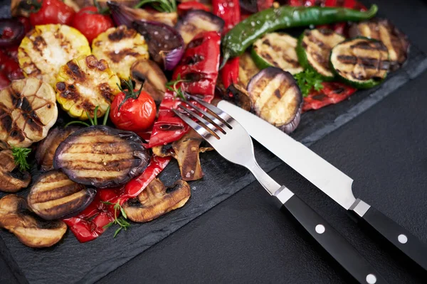 Grilled vegetables mix on a stone serving board - zucchini eggplant onions corn mushroom tomato.