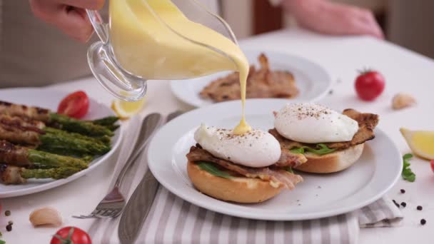卵のベネディクトを作る 女性はポーチドエッグにオランデーズソースを注ぐ — ストック動画