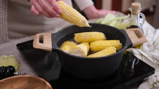 女人在家里的厨房里把玉米芯放进开水里 — 图库视频影像