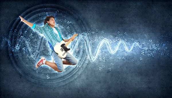 Young man playing on electro guitar and jumping — Stock Photo, Image