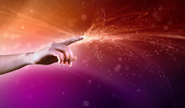 Magical hand conceptual image with sparkles on colour background