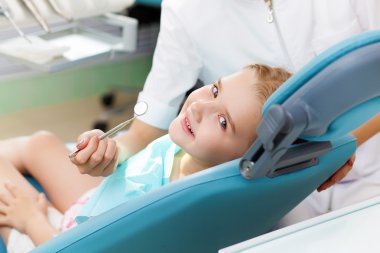 Küçük kız dişçi ofisinde oturuyor.