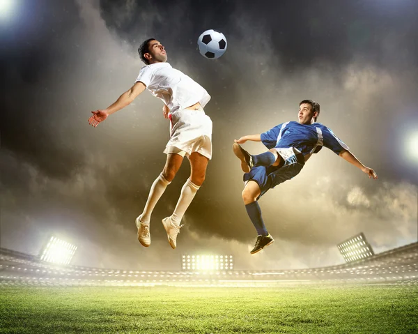 Dos jugadores de fútbol en salto para golpear la pelota en el estadio —  Fotos de Stock