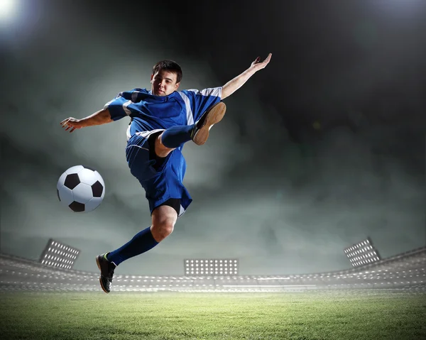 Jogador de futebol em camisa azul golpeando a bola no estádio — Fotografia de Stock