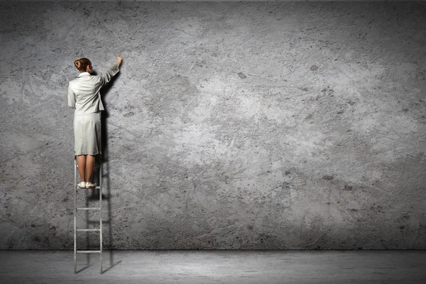 Affärskvinna stående på stege rita diagram och grafer på vägg — Stockfoto