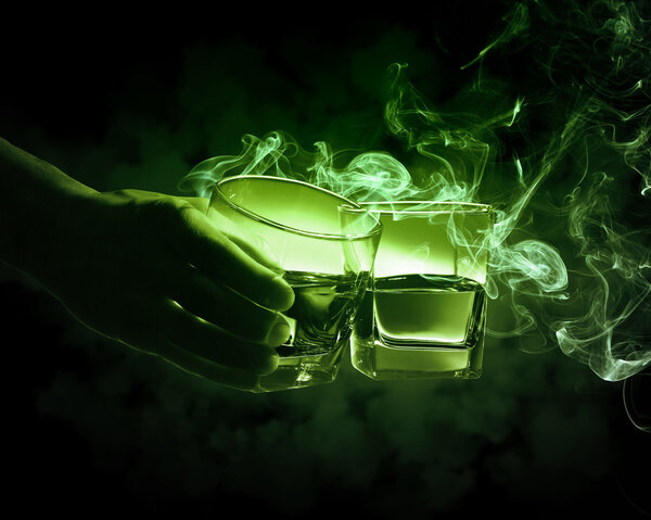 Рука держит один из двух стаканов горящего зеленого абсента
