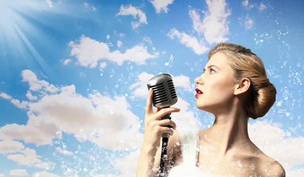 Obrázek blond zpěvačky drží mikrofon pozadí mraků — Stock fotografie