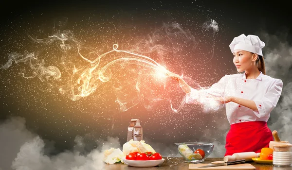 Asian female cooking with magic against color background — Stock Photo, Image
