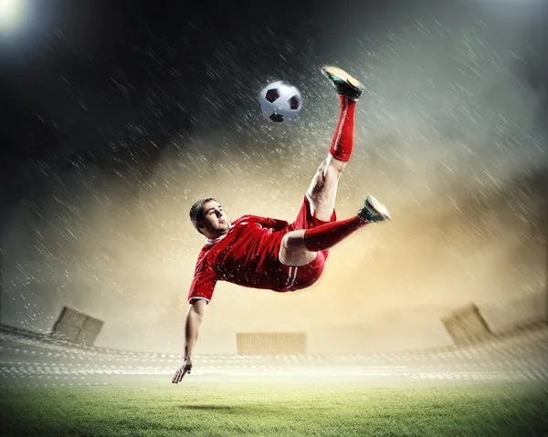 Jogador de futebol em camisa vermelha golpeando a bola no estádio — Fotografia de Stock