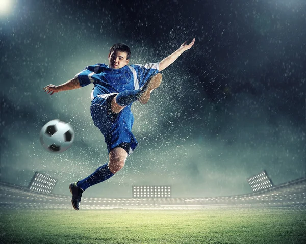 Футболист в синей рубашке бьет по мячу на стадионе — стоковое фото