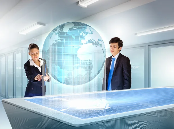 Young businesspeople looking at high-tech image of globe — Stock Photo, Image