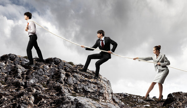 Three businesspeople pulling rope atop of mountain