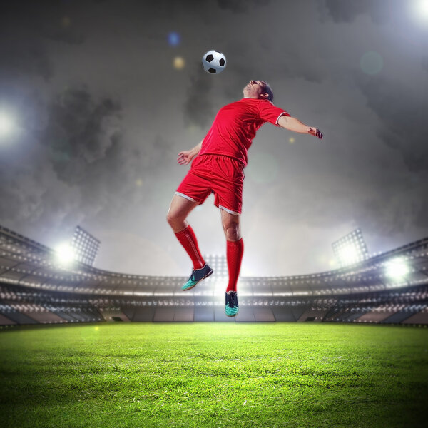 Football player in red shirt striking the ball at the stadium