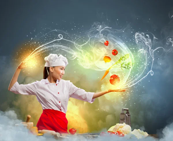 Asian female cooking with magic against color background — Stock Photo, Image