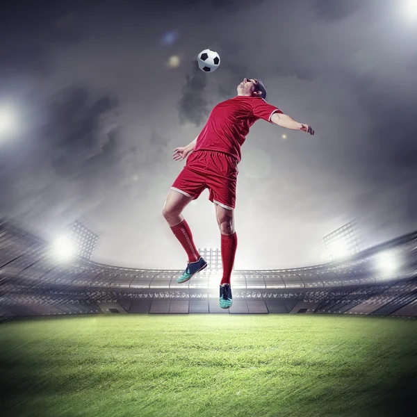 Football player in red shirt striking the ball at the stadium Stock Photo
