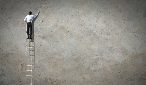 Businessman standing on ladder drawing diagrams and graphs