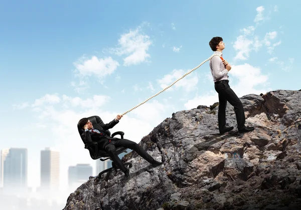 Dos hombres de negocios tirando de la cuerda sobre la montaña — Foto de Stock