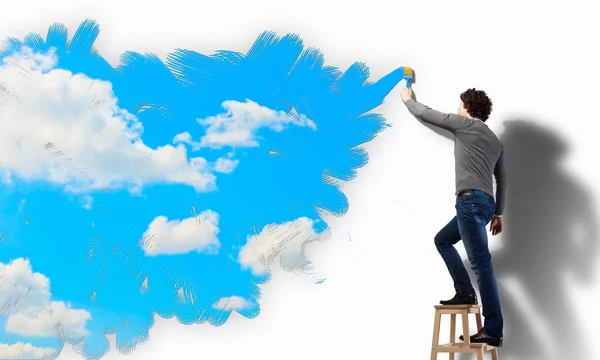 Young man drawing a cloudy blue sky — Stock Photo, Image