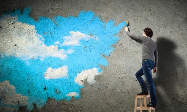 Young man drawing a cloudy blue sky — Stock Photo, Image