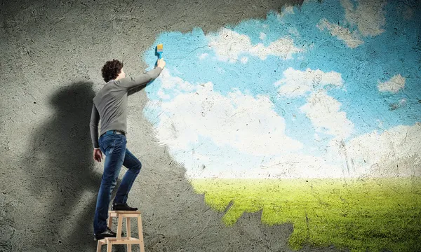 Молодой человек рисует облачно-голубое небо — стоковое фото