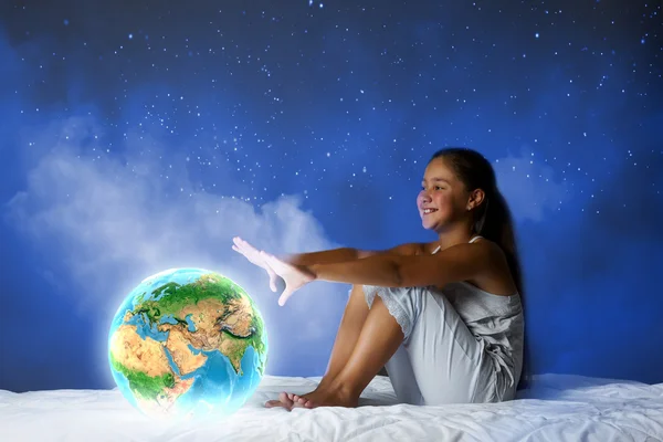 女孩坐在床上，看着地球的行星 — 图库照片